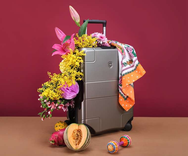 Composition of exotic fruits, flowers around suitcase with metallic finish